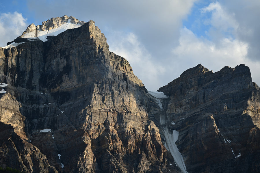 Sunlight and cloud shadows cross steep mountain cliffs.