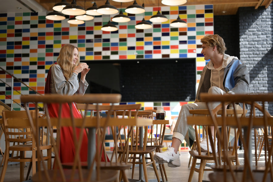 Two people sit across from one another in a café with a colorful tiled wall.