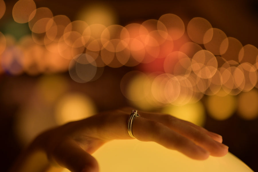A ring rests on a hand silhouetted against warm, softly blurred lights.